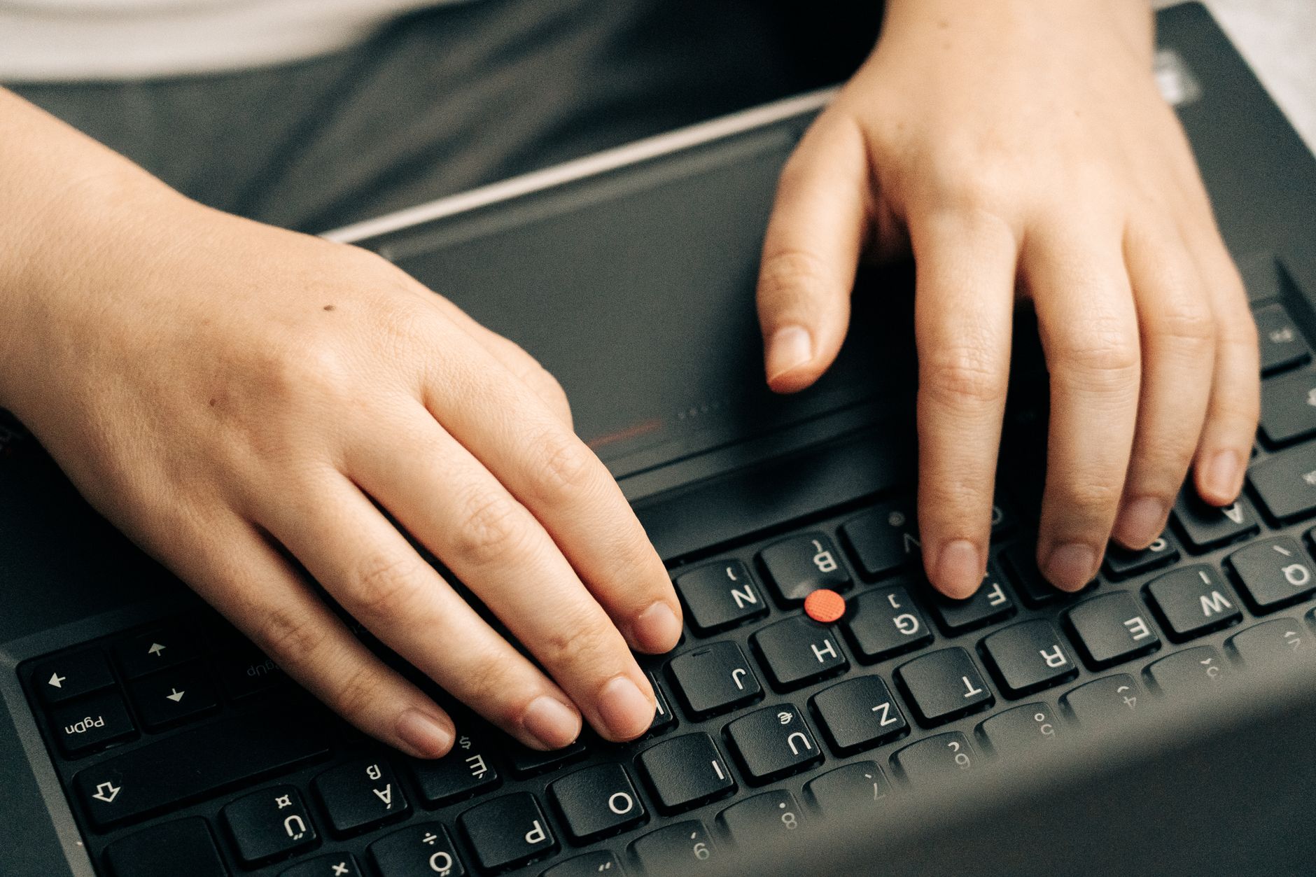 Manos escribiendo en el teclado negro de un portátil, concentradas en una tarea de trabajo digital.
